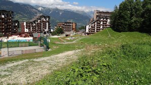 Un complejo turístico de montaña con varios edificios de varios pisos, una piscina y un área verde con un sendero.