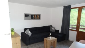 Una sala de estar con un sofá negro, una mesita de madera y una planta en maceta.