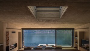 Ein modernes Zimmer mit einer großen Schiebetür, die auf einen See Blick gewährt, einem eingebauten Kamin und einem Flachbildfernseher auf einem Holzboden.