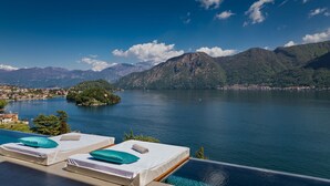 Blick auf ein Schwimmbecken mit Seeblick und Bergen im Hintergrund.