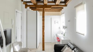 Un salon moderne avec un plafond en bois, un canapé agrémenté de coussins à motifs, un fauteuil blanc et un téléviseur placé à gauche.