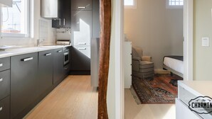 A modern kitchen with grey cabinets, a built-in oven, and a window. A wooden beam ceiling and a small rug are visible.