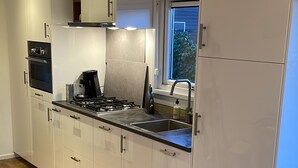A modern kitchen with white cabinetry, a built-in oven, a gas stove, and a window with a view of greenery.