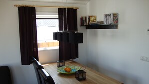 A dining area with a wooden table, chairs, a plate with fruit, a candle holder, and a window with curtains.