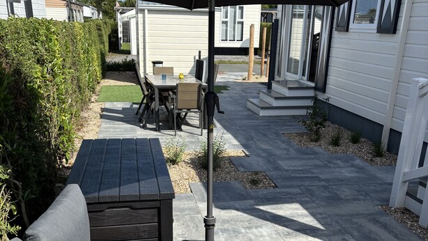 A patio area with a black umbrella, a grey sofa, and a wooden table.