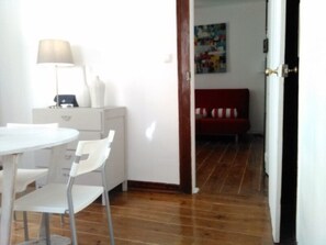 A room with a round dining table, two white chairs, a lamp, a white cabinet, and a red sofa.
