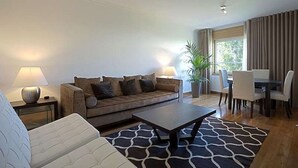 A living room with a sofa, coffee table, and dining area with chairs and a table. - GREEN ÁVILA (LISBOA)