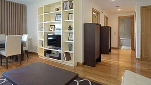 A living room with a white bookshelf, a dark-colored sofa, a flat-screen TV, and a wooden floor. - GREEN ÁVILA (LISBOA)