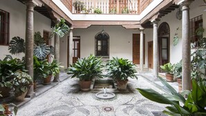 A courtyard with a central fountain, surrounded by potted plants and columns.