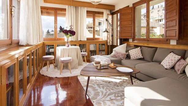 A cozy living room with a wooden floor, a sofa, a coffee table, and a view of the city through large windows.