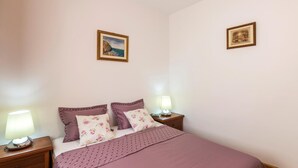 Ein ordentlich bezogenes Bett mit einer rosa Bettdecke und floralen Kissen, zwei Nachttischlampen und zwei gerahmte Bilder an den Wänden.