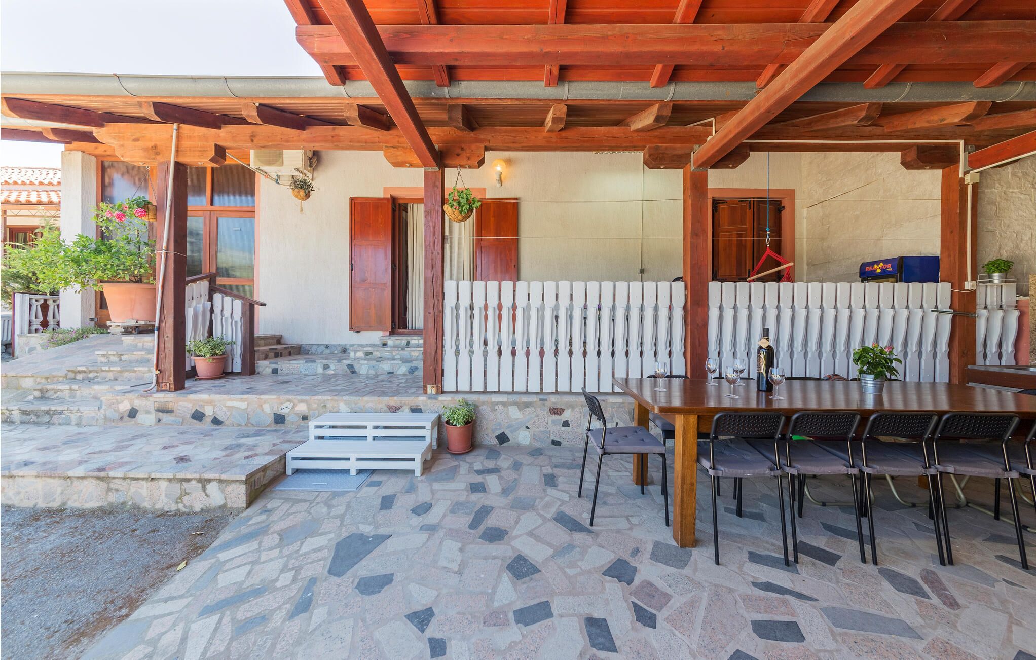 Une terrasse extérieure dotée d’une pergola en bois, d’un revêtement de sol en pierre et d’un espace repas avec des tables et des chaises.