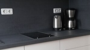 A modern kitchen with white cabinets, a black countertop, a coffee maker, and a built-in oven. - Apartment in Bansin (Seebad Bansin)