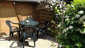An outdoor patio with a round table and four chairs, surrounded by a wooden fence and flowering plants. - Apartment in Bansin (Seebad Bansin)