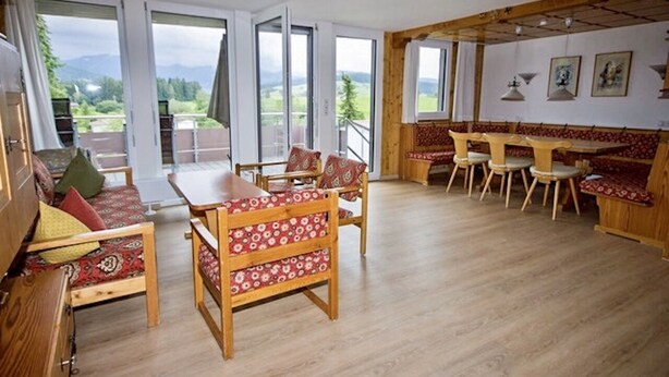 Ein gemütliches Zimmer mit Holzboden, einer Couch, einem Esstisch mit Stühlen und einem Balkon mit Bergblick.