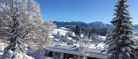 A snow-covered landscape with a house in the foreground and mountains in the background.