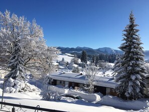 A snow-covered landscape with a house in the foreground and mountains in the background.