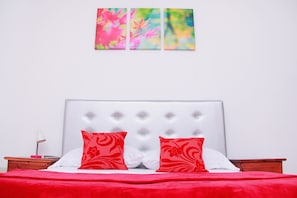 A bed with red bedding and white pillows, a white headboard, and a nightstand with a lamp.