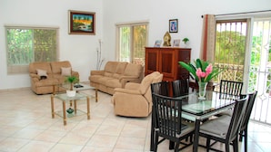 Ein Wohnzimmer mit beigen Sofas, einem Glastisch und einem Essbereich mit Tisch und Stühlen.