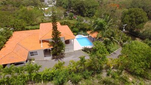 An aerial view of a house with a tiled roof, a swimming pool, and surrounding greenery.