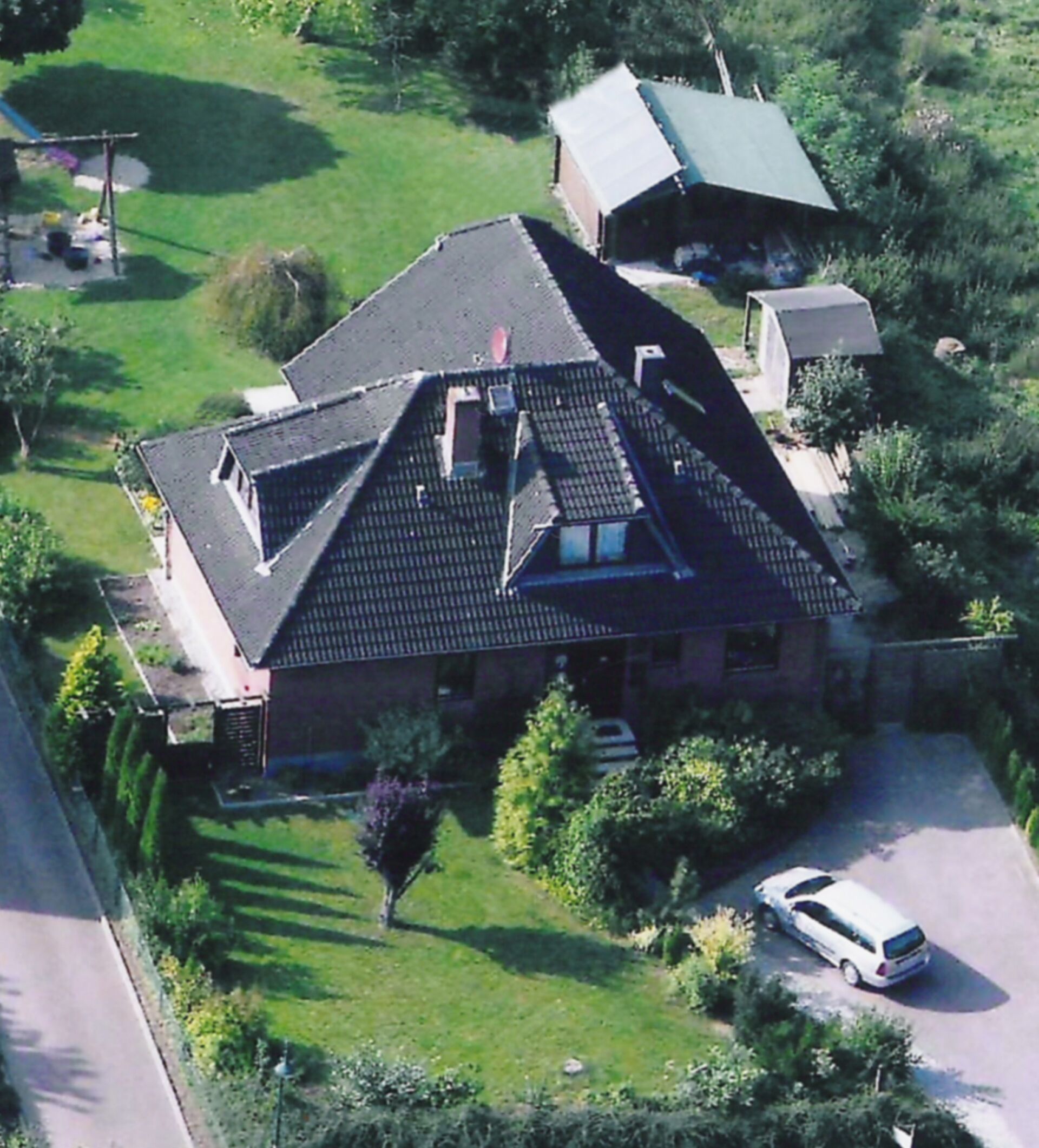 Une maison de plain-pied avec un toit en pente, une cheminée bien visible et une allée où est garée une voiture.