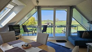 Un dormitorio tipo loft moderno con un tragaluz grande, un balcón con mobiliario exterior y vistas a un paisaje verde.