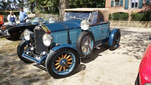 Un coche azul antiguo con techo descapotable estacionado sobre una superficie de tierra.
