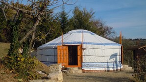 A traditional yurt with a wooden door and a patterned design, surrounded by natural vegetation and a gravel path. - Convert your vacation into a highly regenerating life experience. (Pontassieve)