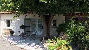 A building with a patio area featuring a table and chairs, a potted plant, and a tree providing shade. - QUIET 8-BED FAMILY HOME WITH SWIMMING POOL (st martin de villeréglan)