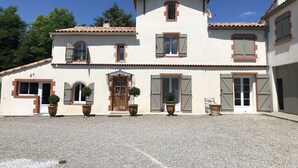 A two-story building with a symmetrical facade, featuring a central entrance with a decorative archway, multiple windows with shutters, and a satellite dish on the roof. - QUIET 8-BED FAMILY HOME WITH SWIMMING POOL (st martin de villeréglan)