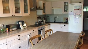 A modern kitchen with white cabinets, a wooden dining table, and basic appliances. - QUIET 8-BED FAMILY HOME WITH SWIMMING POOL (st martin de villeréglan)