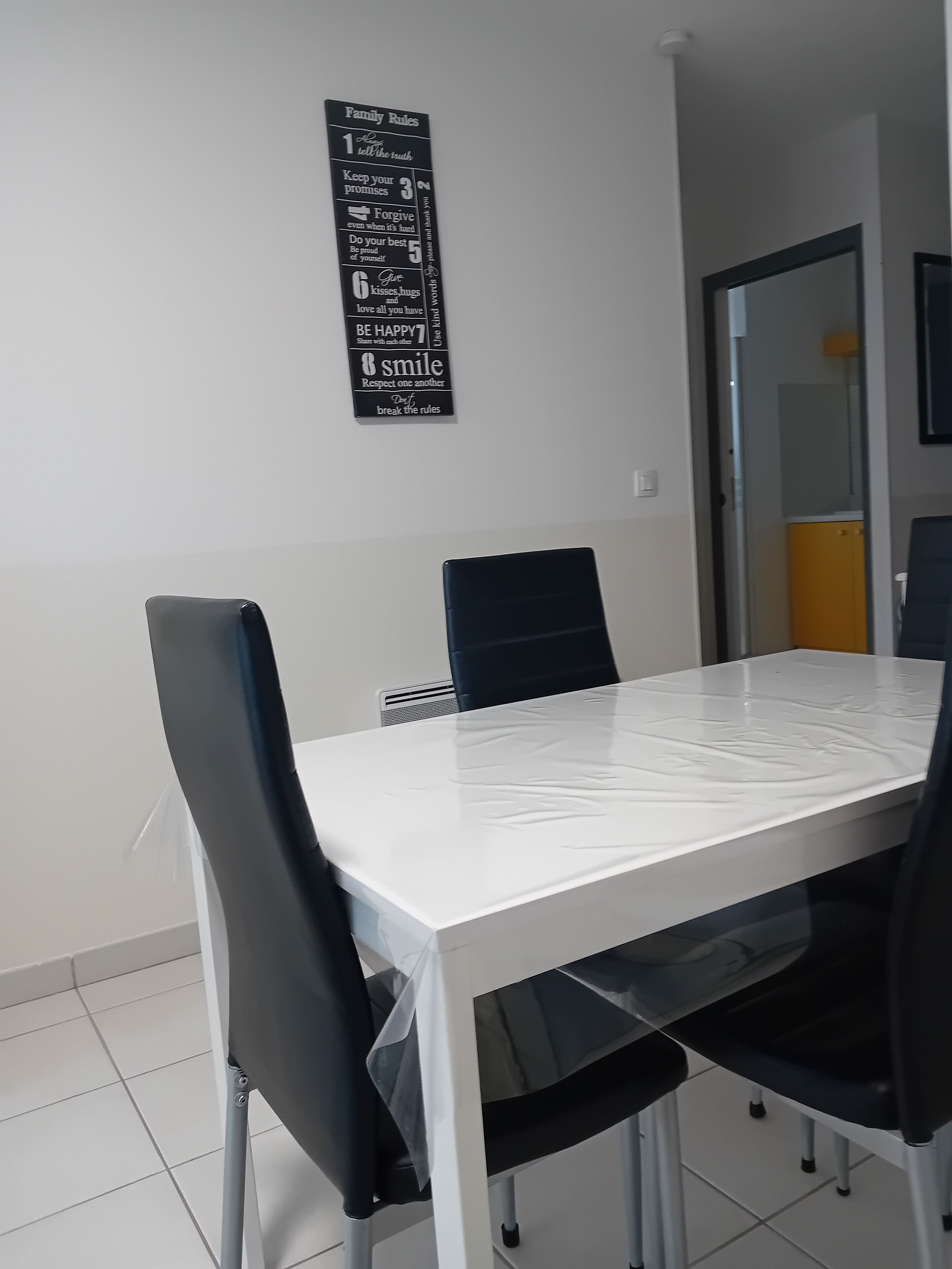 Une salle de conférence avec une table blanche, des chaises noires et un panneau affichant les règles familiales, fixé au mur.