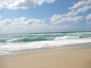 A beach with waves crashing onto the shore under a partly cloudy sky.