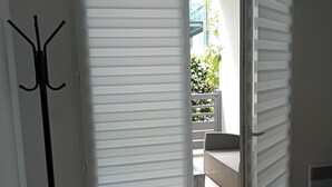Ein Zimmer mit einem Bett, einem Kleiderhaken und einer Schiebetür zu einem Außenbereich mit einer Bank und Bepflanzung.