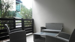 Eine Terrassenfläche mit Korbmöbeln, darunter Stühle und eine Sitzecke, sowie einem Tisch mit Glasplatte.