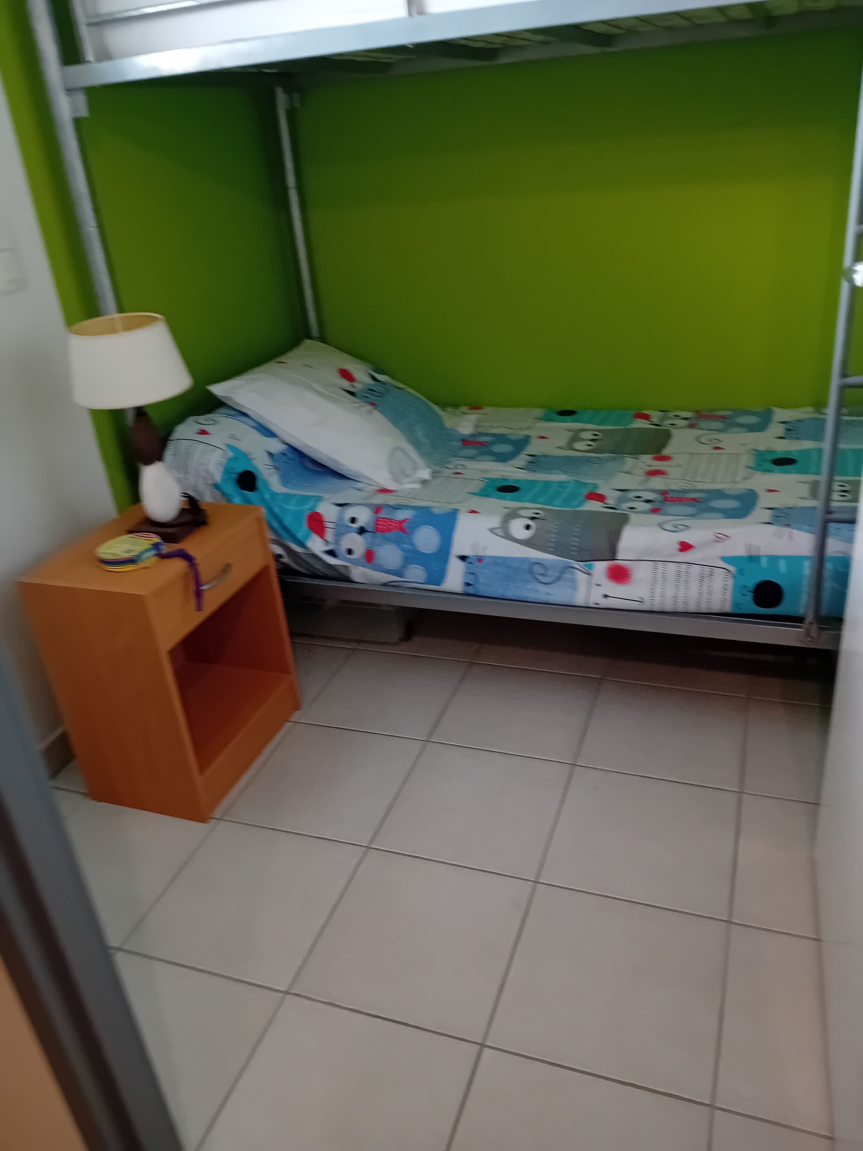 Una stanza piccola e compatta con un letto a castello, un comodino con una lampada e una parete verde.