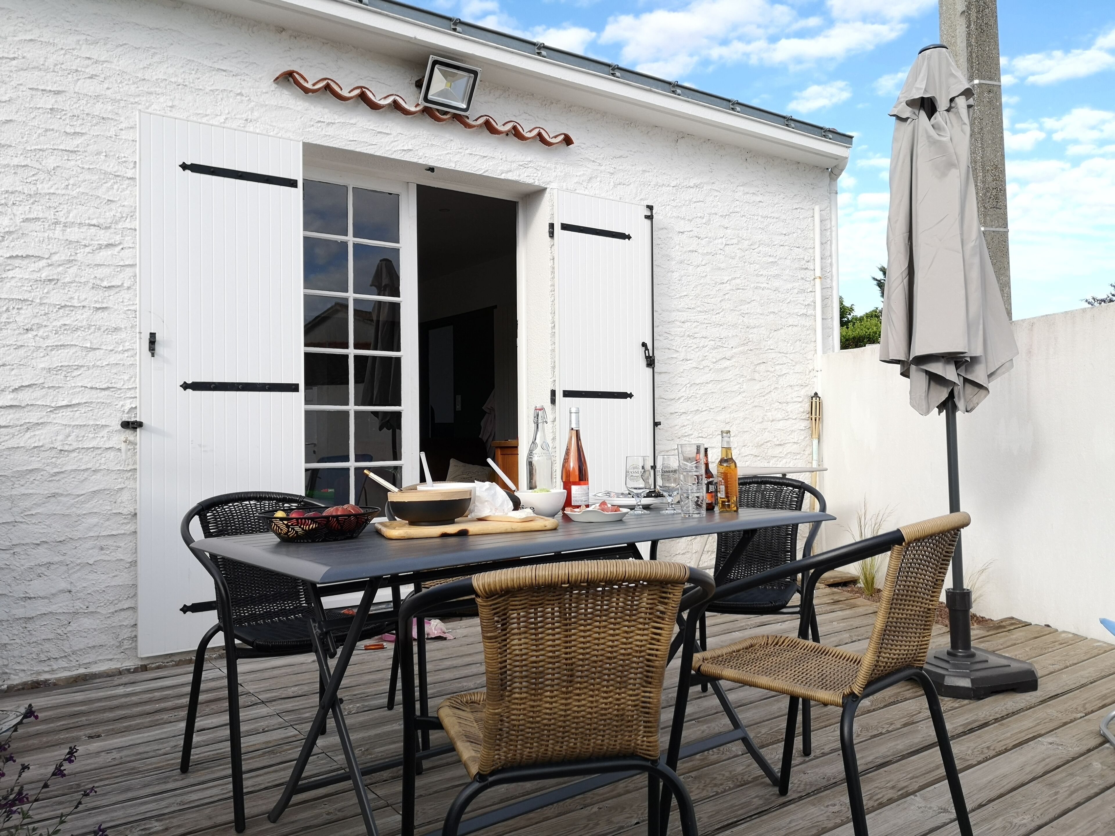 An outdoor dining area with a white building, a table set with chairs, and a pergola with a canopy.