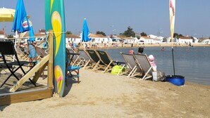 A beach with wooden chairs and umbrellas, a water body, and buildings in the background. - 2-bedroom house, close to the beach, all on foot (L'aiguillon-Sur-Mer)