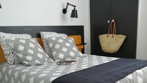 A neatly made bed with patterned bedding, a dark throw blanket, and a wall-mounted lamp. - 2-bedroom house, close to the beach, all on foot (L'aiguillon-Sur-Mer)