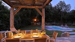 Zona d'esmorzar a l'aire lliure amb una pèrgola de fusta, una piscina i gandules.