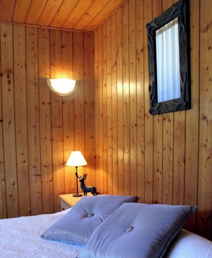 Ein Holzhüttenraum mit einem Bett, einem Nachttisch mit Lampe und einer Hirschfigur.