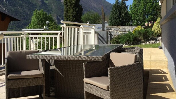 An outdoor patio with wicker furniture, a glass-top table, and a view of mountains.