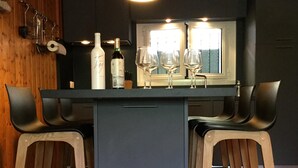 A bar area with a central island, two stools, a hanging light fixture, and a window with a view.