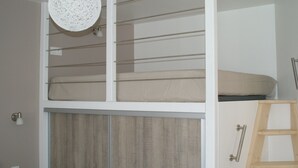Een stapelbed met hoofdeinde, een houten ladder en een witte muur met een lamp.