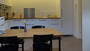 Een moderne keuken met een eettafel, stoelen, een hanglamp en een koelkast.