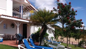 Ein Gebäude mit Balkon, einer Sitzgelegenheit im Freien mit blauen und weißen Lounge-Stühlen sowie ein Baum mit roten Blüten.