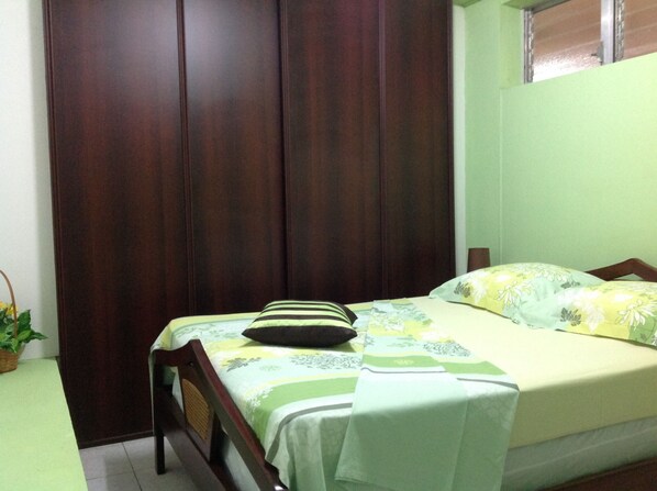 Une chambre à coucher avec un lit, une armoire en bois, une fenêtre et une petite table sur laquelle est posée une plante.