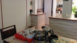 Eine Küche mit Essbereich, ausgestattet mit einem Tisch, Geschirr und Kochtöpfen, einer roten Aufbewahrungsbox und einem Kühlschrank.