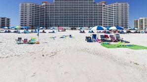 A beachfront hotel with multiple balconies, beach umbrellas, and lounge chairs. - Beach Front Condo, Spacious, Clean and Comfortable (Gulf Shores)