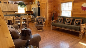 A cozy log cabin interior with a wooden dining table, a sofa with moose-themed cushions, and a glass coffee table with a bear figurine. - Big Nate Cabin on Lake with Water Trampoline (Hiawassee)